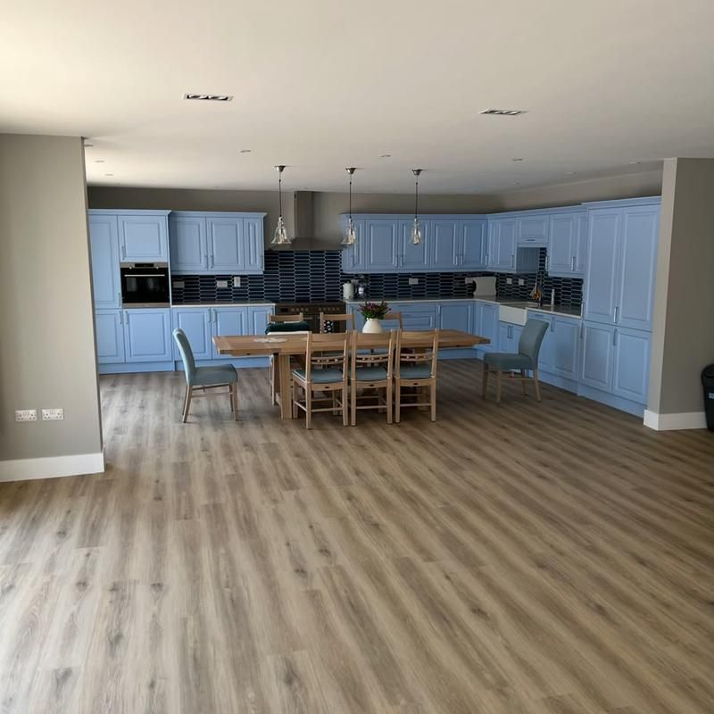Wide view of the open kitchen-diner with blue cabinetry and a long dining table