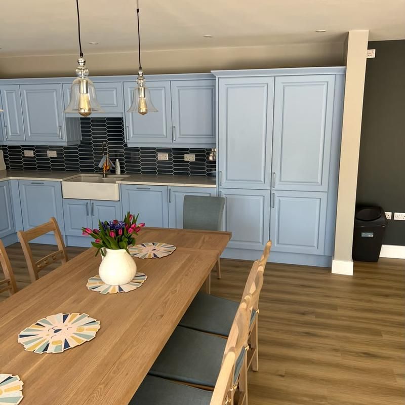 Timber dining table in front of blue kitchen units and pendant lights