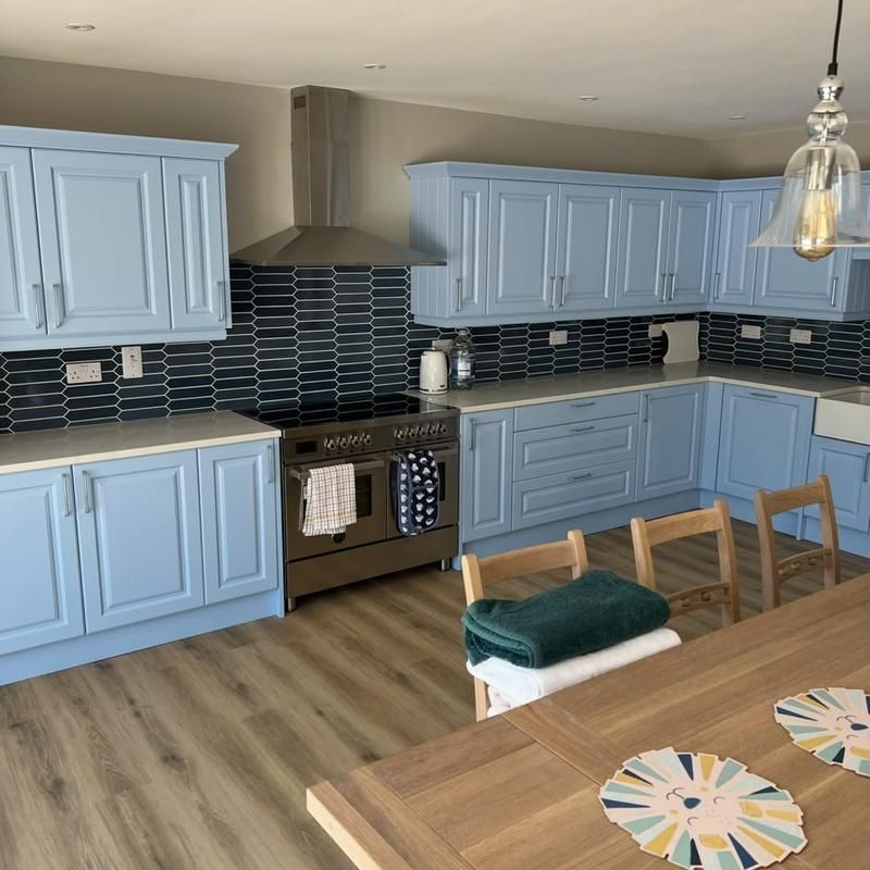 Blue kitchen units with a range cooker and dark splashback tiles