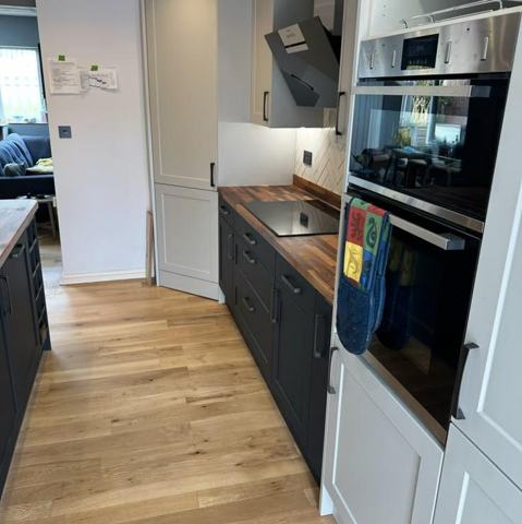 Dark shaker units, stacked ovens and timber worktops above an oak floor