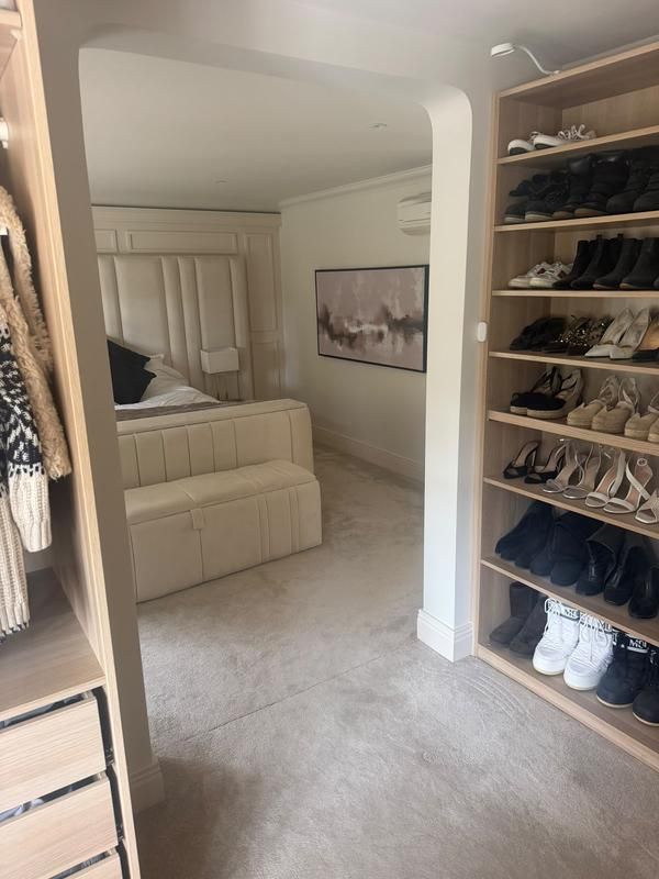 Floor-to-ceiling shoe shelving beside a cream bed