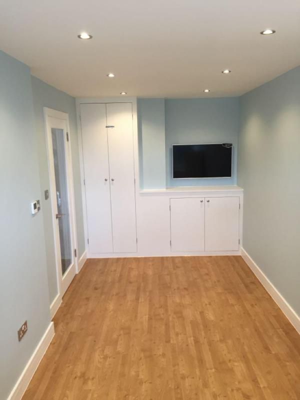 Converted garage finished as a room with timber-effect flooring, fitted cupboards and a wall-mounted TV
