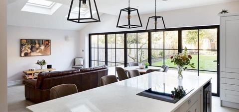 Bright open-plan kitchen with a white island, pendant lights and black-framed glazing